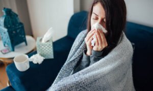 Sick woman blowing her nose, she covered with blanket